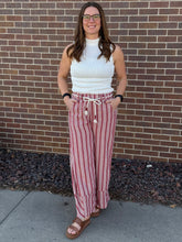 Load image into Gallery viewer, Woman wearing a white top and red striped pants standing against a brick wall.