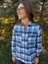 Load image into Gallery viewer, Woman wearing a blue plaid shirt standing outdoors with trees in the background