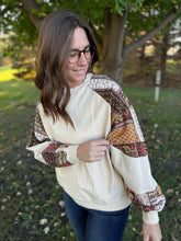 Load image into Gallery viewer, Woman wearing a cream-colored sweatshirt with patterned sleeves outdoors.