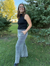 Load image into Gallery viewer, Woman in black sleeveless top and gray wide-leg pants standing outdoors with trees in the background