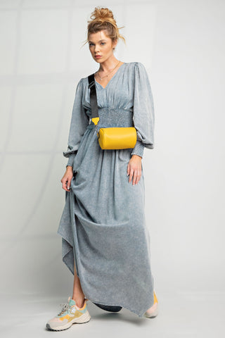 Woman wearing a long gray dress with a yellow bag on a plain background
