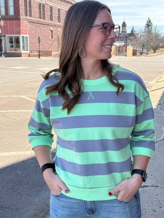 Woman wearing a green and purple striped sweater in an outdoor setting.