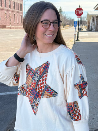 Woman wearing a white sweater with colorful star patterns on a street.