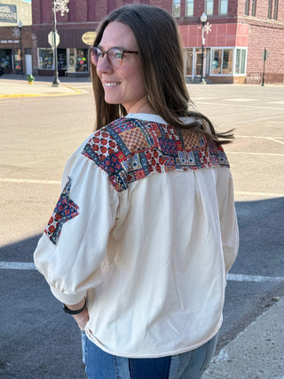 Woman wearing a white blouse with colorful patchwork patterns on a city street.