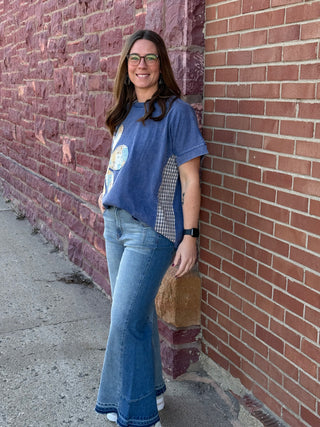 Woman leaning against a brick wall wearing a blue shirt and jeans.