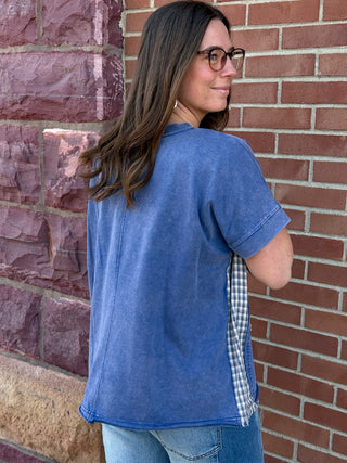 Woman wearing a blue shirt with plaid trim against a brick wall
