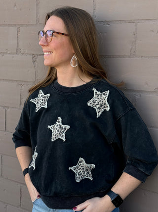 Woman wearing a black sweatshirt with star patterns against a brick wall.