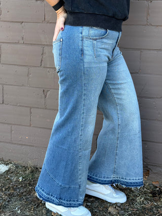 Person wearing blue flared jeans standing against a brick wall.