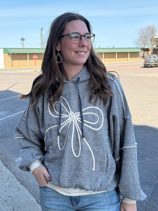 Woman wearing a gray hoodie with a white bow design in an outdoor setting