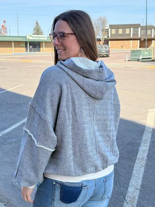 Woman wearing a gray hoodie and blue jeans standing in a parking lot.