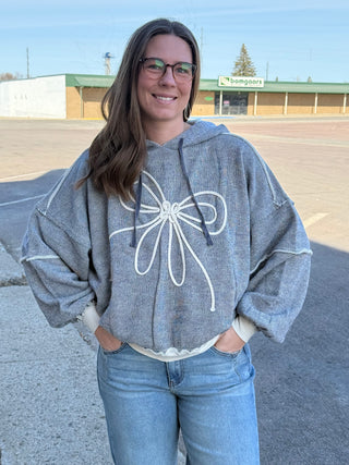 Woman wearing a gray hoodie with a white butterfly design in an outdoor setting.