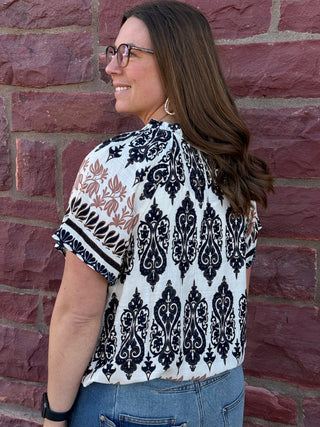 Woman wearing a patterned blouse standing against a brick wall