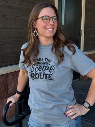 Woman wearing a t-shirt with 'Take the Scenic Route' text, standing outdoors.