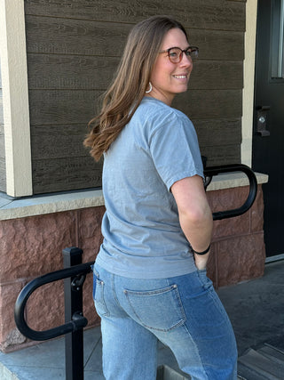 Woman wearing a blue t-shirt and jeans standing outside a building.