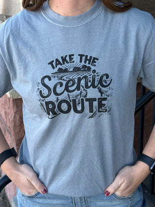 Person wearing a light blue t-shirt with 'Take the Scenic Route' text design.