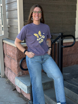 Woman wearing a purple t-shirt with a butterfly design on steps outside a house