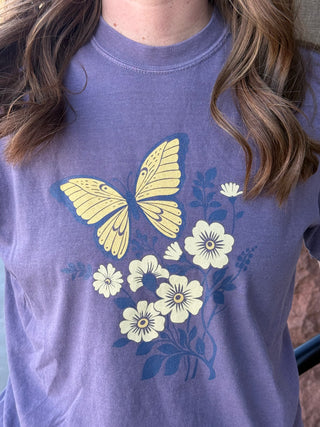 Purple t-shirt with yellow butterfly and flower design worn by a person.