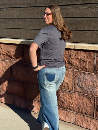 Woman wearing a gray t-shirt and blue jeans standing against a brick wall.