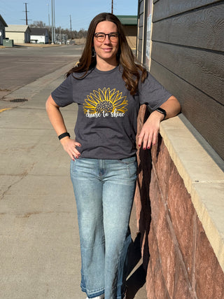 Woman wearing a t-shirt with a sunflower design and text, standing outdoors.