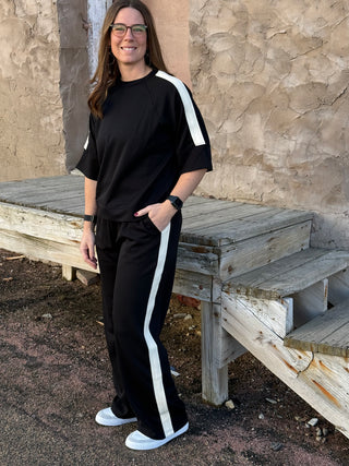 Woman wearing a black outfit with white stripes standing next to a wooden bench.