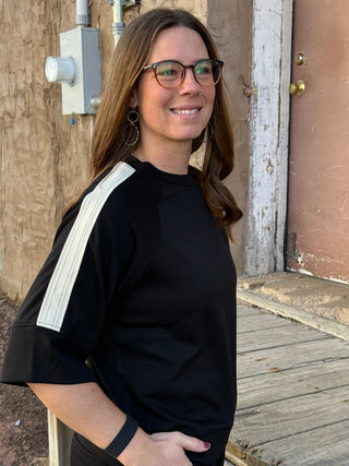 Woman wearing a black top with white stripes standing outside a building.