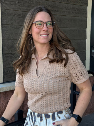 Woman wearing a beige knit top and patterned skirt sitting outdoors.