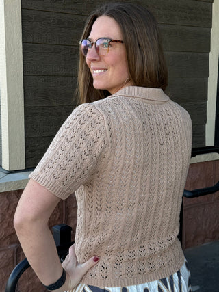 Woman wearing a beige knitted cardigan standing outdoors.