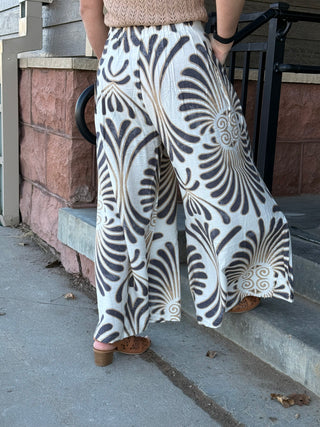 Person wearing patterned pants standing on a sidewalk.