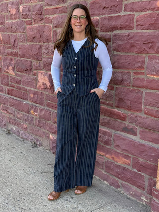 Woman wearing a navy pinstripe outfit standing against a brick wall.