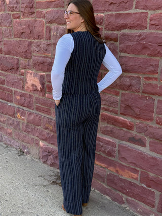 Woman wearing a black pinstripe jumpsuit against a brick wall.