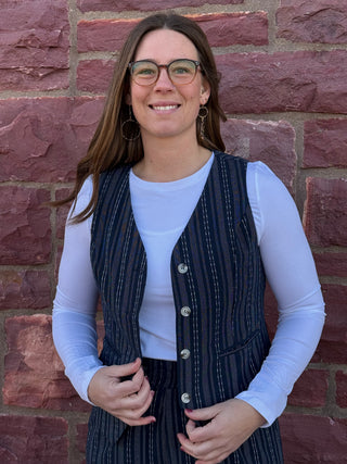 Woman wearing a striped vest over a white shirt against a brick wall.