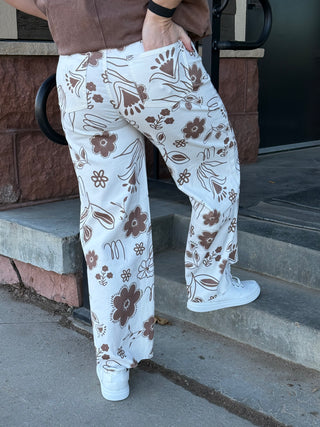 Person wearing white pants with brown floral patterns, standing on steps.