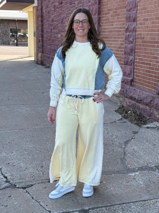 Woman wearing a light-colored outfit with a denim jacket against a brick wall.