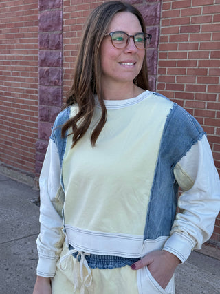 Woman wearing a light-colored sweatshirt with denim sleeves against a brick wall.
