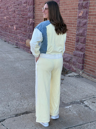 Woman wearing a light-colored outfit with denim accents against a brick wall.