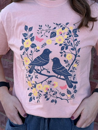 Person wearing a pink t-shirt with a bird and floral design.