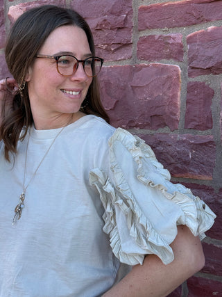 Woman wearing a light blue blouse with ruffled sleeves against a brick wall.