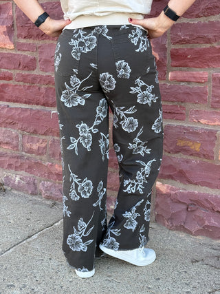 Person wearing black floral pants standing against a brick wall.
