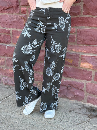 Person wearing black floral pants standing against a brick wall.
