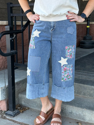 Person wearing blue patchwork jeans with floral and star patterns, standing on steps.