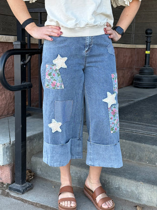 Person wearing blue denim capri pants with floral and star patches on a staircase.