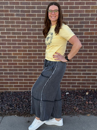 Woman wearing a yellow t-shirt and blue jeans standing in front of a brick wall.