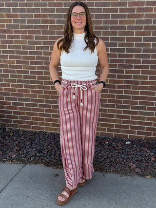 Woman wearing a white top and red striped pants standing against a brick wall.