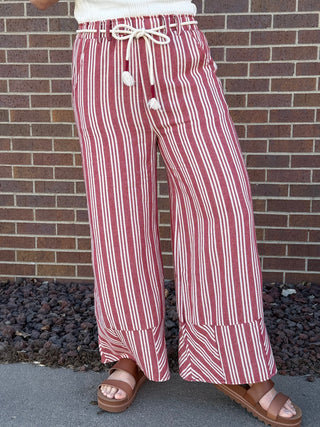Person wearing red and white striped pants standing against a brick wall.