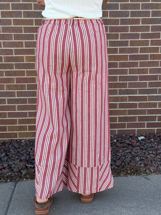 Person wearing red and white striped pants standing against a brick wall.