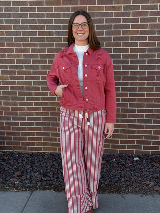Woman wearing a red jacket and striped pants standing in front of a brick wall.