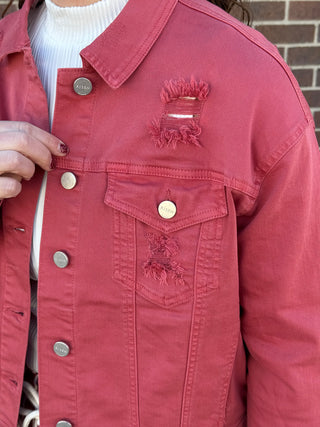 Close-up of a red denim jacket with distressing on a brick wall background