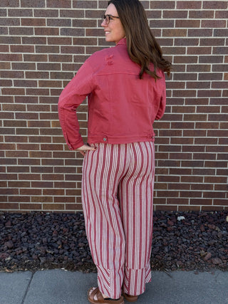 Woman wearing a red jacket and striped pants standing against a brick wall.