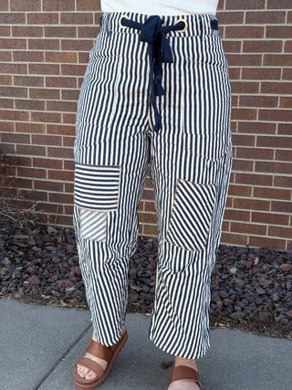 Person wearing black and white striped pants with patch pockets against a brick wall.