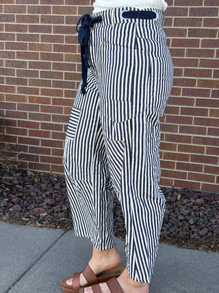 Person wearing black and white striped pants standing against a brick wall.